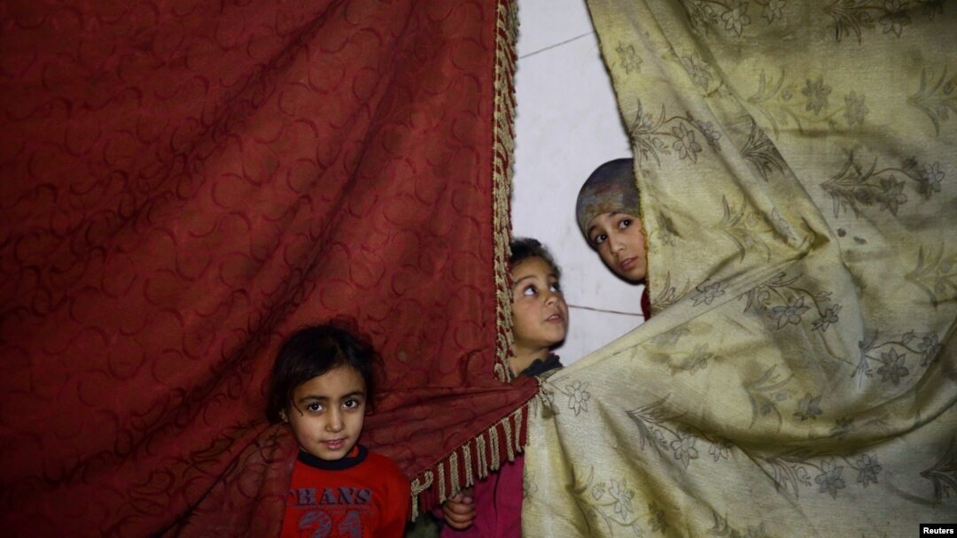 Anak-anak berdiri dekat tirai-tirai di sebuah tempat perlindungan di Douma, sebuah kota yang terkepung di timur Ghouta, di Damaskus, Suriah, 11 Maret 2018. 