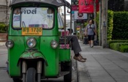 FILE - A tuk-tuk driver naps as a man walks past in an area usually busy with tourists in Bangkok, Thailand, Aug. 27, 2020. The pandemic, with its damage to the tourism industry, has hit the Thai economy hard.