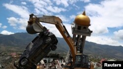 Excavator memindahkan mobil dekat reruntuhan sebuah masjid akibat gempa di daerah Balaroa, Palu, Sulawesi Tengah (8/10).