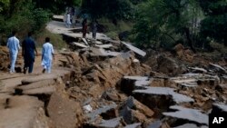 Residents walk alongside a damaged portion of a road caused by a powerful earthquake in Jatlan near Mirpur, in northeast Pakistan.