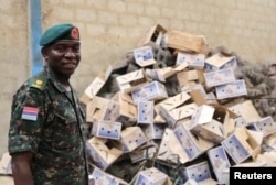 Gambian Major YMS Darboe stands in front of a pile of empty cardboard boxes stored in a warehouse in former Gambian President Yahya Jammeh's personal estate in Kanilai, Gambia, July 1, 2017.