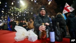 A man opens a drink as other people gather in a street decorated for Christmas and the New Year festivities on New Year's Eve outside of the Georgian parliament, in Tbilisi, Georgia, Dec. 31, 2024.