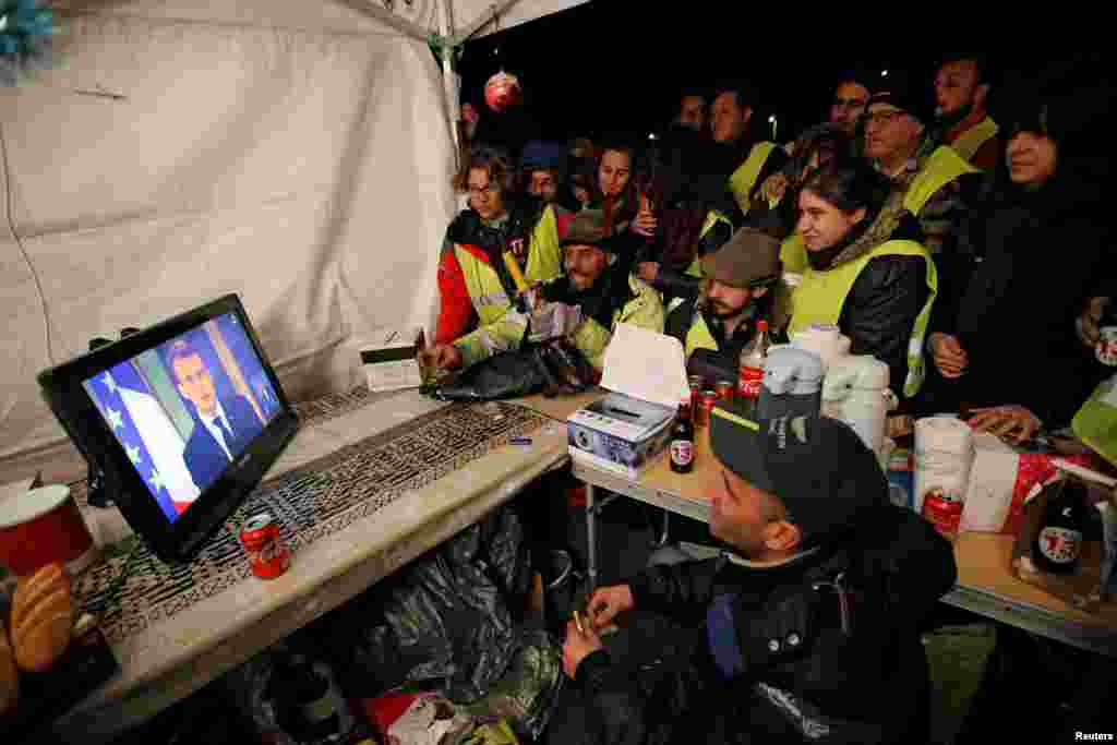 Protesters wearing yellow vests watch French President Emmanuel Macron on TV at the motorway toll booth in La Ciotat, near Marseille, France, December 10, 2018.