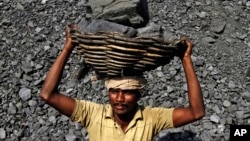 FILE - an Indian daily wage laborer carries a basket on his head filled with chunks of coal at a local coal depot on the outskirts of Cuttack, India, Nov. 13, 2014. 