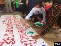 ស្រ្តីម្នាក់ កំពុង​ផ្តិត​បាតដៃ​នឹង​ថ្នាំពណ៌​លើ​ផ្ទាំង​ក្រណាត់​ដែល​មាន​សរសេរ​ពាក្យស្លោក ក្នុង​ទិវា​អន្តរជាតិ​«បញ្ឈប់​ការប្រើប្រាស់​អំពើ​ហិង្សា​លើ​អ្នករកស៊ី​ផ្លូវភេទ» នៅ​ខណ្ឌឫស្សីកែវ រាជធានី​ភ្នំពេញ នៅ​ថ្ងៃទី១៦ ខែធ្នូ ២០២១។ (មាស មល្លិកា/វីអូអេ)