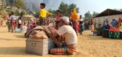 Rohingya refugees salvage their belongings and watch smoke rising following a fire at the Rohingya refugee camp in Balukhali, southern Bangladesh, March 22, 2021.