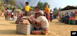Rohingya refugees salvage their belongings and watch smoke rising following a fire at the Rohingya refugee camp in Balukhali, southern Bangladesh, March 22, 2021.