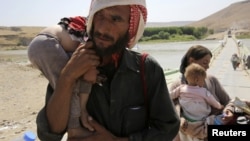 A man and his wife from the minority Yazidi sect, fleeing the violence in the Iraqi town of Sinjar, carry their children as they re-enter Iraq from Syria at the Iraqi-Syrian border crossing in Fishkhabour, Dohuk province, August 14, 2014.