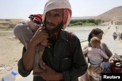 A man and his wife from the minority Yazidi sect, fleeing the violence in the Iraqi town of Sinjar, carry their children as they re-enter Iraq from Syria at the Iraqi-Syrian border crossing in Fishkhabour, Dohuk province, August 14, 2014.