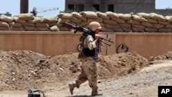 FILE - A Kurdish peshmerga fighter carries his weapon walks onto his base at the front line in Tuz Khormato, 100 kilometers (62 miles) south of Kirkuk, northern Iraq. June 25, 2014.