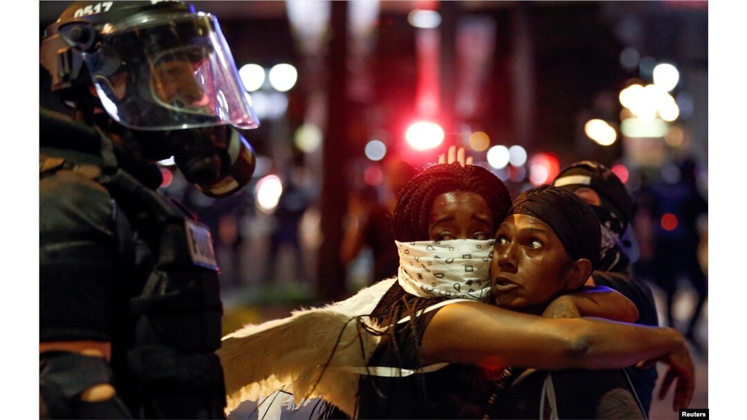 Two women embrace while looking at a police officer in uptown Charlotte, during a protest of the police shooting of Keith Scott, in Charlotte, North Carolina, Sept. 21, 2016.