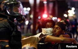 Two women embrace while looking at a police officer in uptown Charlotte, during a protest of the police shooting of Keith Scott, in Charlotte, North Carolina, Sept. 21, 2016.