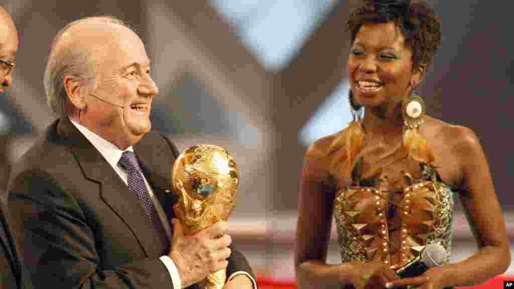 FIFA President Sepp Blatter holds aloft the trophy watched by show host Carol Manana during the 2010 World Cup draw in Cape Town, South Africa, December 4, 2009.