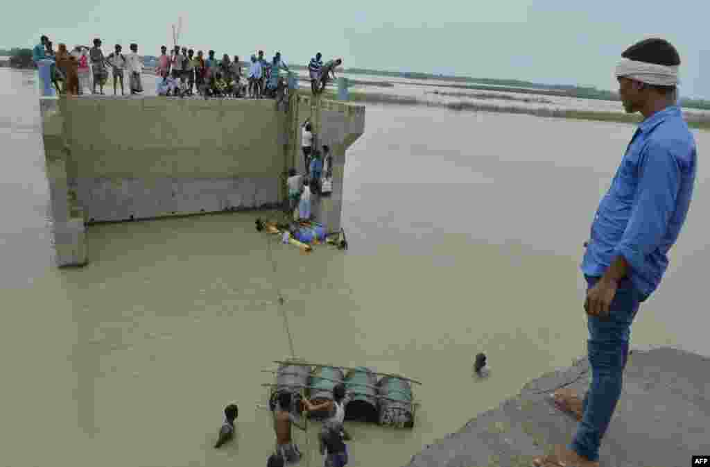 Indian villagers attempt to cross flood waters with the help of rope and empty canisters next to a washed away portion of a bridge at Palsa village in Purnia district in Bihar state.