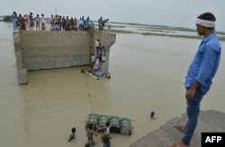 Indian villagers attempt to cross flood waters, Aug. 18, 2017, with the help of rope and empty canisters next to a washed away portion of a bridge at Palsa village in Purnia district in Bihar state.