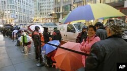 Apple customers use umbrellas as they wait in line at an Apple store on the first day of the launch of the new iPad, in San Francisco, March 16, 2012. 