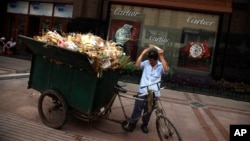 FILE - A man prepares to push a garbage cart near a shop selling luxury watches along a shopping street in Beijing, China, Aug. 3, 2010. Many of China's richest have embraced the philosophies of western capitalists who turned to philanthropy.