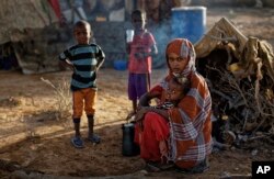 In this photo taken Thursday, March 9, 2017, Fatima Ali and her children, who fled the drought, sit by their makeshift hut in a camp for the displaced in Qardho in Somalia's semiautonomous northeastern state of Puntland.