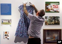 A gallery stylist hangs a dress, fashioned with polka dots and Winnie the Pooh characters, while preparing a display at the "Winnie-the-Pooh: Exploring a Classic" exhibit at the Museum of Fine Arts in Boston, Sept. 13, 2018.