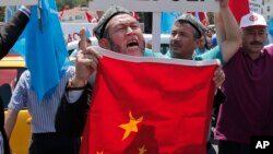 FILE - Uighurs living in Turkey and Turkish supporters, chant slogans as they hold a Chinese flag before burning it during a protest near China's consulate in Istanbul, against what they call oppression by Chinese government to Muslim Uighurs in far-western Xinjiang region, July 5, 2015. 