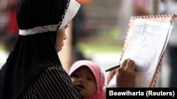 Seorang ibu sedang menggendong bayinya saat mengisi formulir lamaran kerja saat job expo di Batam 18 September 2006, sebagai ilustrasi. (Foto: REUTERS/Beawiharta)