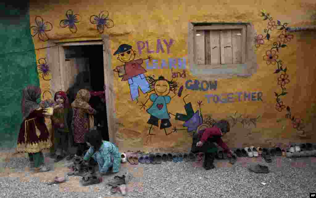 Anak-anak sekolah mencari-cari sepatunya sementara yang lain masuk kelas di tengah kunjungan petugas vaksin polio ke daerah miskin di pinggir kota Islamabad (31/1). (AP/Muhammad Muheisen)