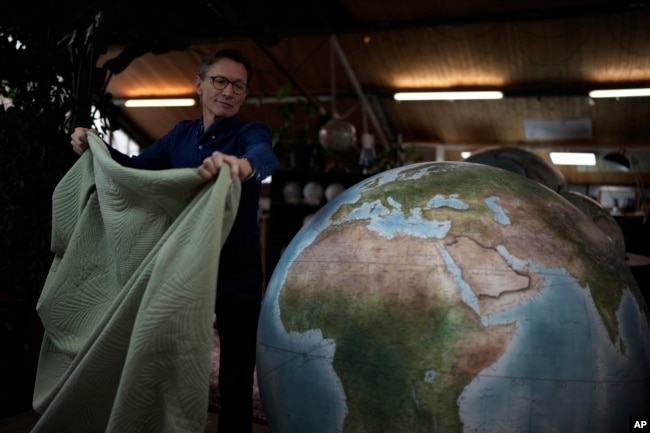 Peter Bellerby, the founder of Bellerby & Co. Globemakers, covers a globe at his studio in London, Tuesday, Feb. 27, 2024. (AP Photo/Kin Cheung)