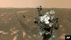 File- April 6, 2021 image made available by NASA shows the Perseverance Mars rover, foreground, and the Ingenuity helicopter about 13 feet (3.9 meters) behind.