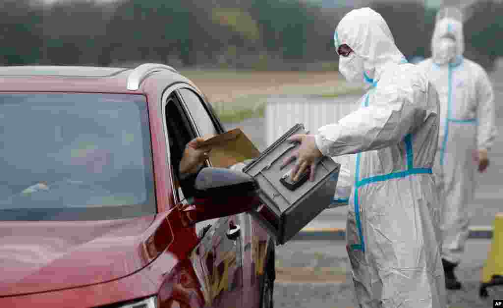 An election committee member, wearing a protective suit, holds a ballot box for a man to vote in regional and senate elections, at a drive-in polling station in Prague, Czech Republic.