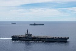 FILE - In this photo provided by U.S. Navy, the USS Ronald Reagan (CVN 76, front) and USS Nimitz (CVN 68, rear) Carrier Strike Groups sail together in formation, in the South China Sea, July 6, 2020.
