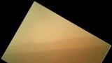 This image shows the first color view of the north wall and rim of Gale Crater where Curiosity landed. The picture was taken by the rover's camera at the end of its stowed robotic arm and appears fuzzy because of dust on the camera's cover. 