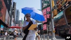 A woman uses an umbrella to block out the sun while walking through Times Square, July 20, 2019, in New York.