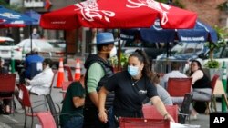 Una camarera atiende a los clientes en un restaurante con comidas al aire libre en una sección de la calle cerrada al tráfico para promover el distanciamiento social, el viernes 17 de julio de 2020, en Somerville, Massachusetts.