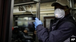 FILE - A New York subway rider wears protective gloves and a mask while holding onto a pole, March 19, 2020.