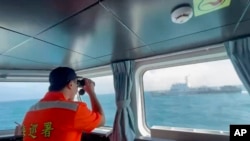 In this screen grab from video released by the Taiwan Coast Guard, a member of the Taiwan Coast Guard monitors a China Coast Guard boat as it passes near the coast of Matsu islands, Taiwan, Oct. 14, 2024. (Taiwan Coast Guard via AP)