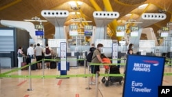 Passengers wearing face masks to prevent the spread of coronavirus queue prior to departure to London at a British Airways check-in desk at Adolfo Suarez-Barajas international airport, outskirts Madrid, Spain, Sunday, July 26, 2020. Britain has put…