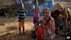 In this photo taken Thursday, March 9, 2017, Fatima Ali and her children, who fled the drought, sit by their makeshift hut in a camp for the displaced in Qardho in Somalia's semiautonomous northeastern state of Puntland.