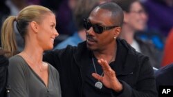 Actor Eddie Murphy talks with his girlfriend Paige Butcher during an NBA basketball game between the Los Angeles Lakers and the Dallas Mavericks, April 12, 2015, in Los Angeles. 
