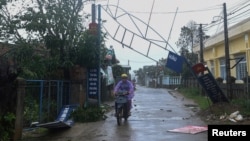 A man bikes past a broken sign as the Typhoon Molave lashes Vietnam's coast in Binh Chau village, Quang Ngai province, Oct. 28, 2020. 