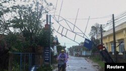 A man bikes past a broken sign as the Typhoon Molave lashes Vietnam's coast in Binh Chau village, Quang Ngai province, Oct. 28, 2020. 