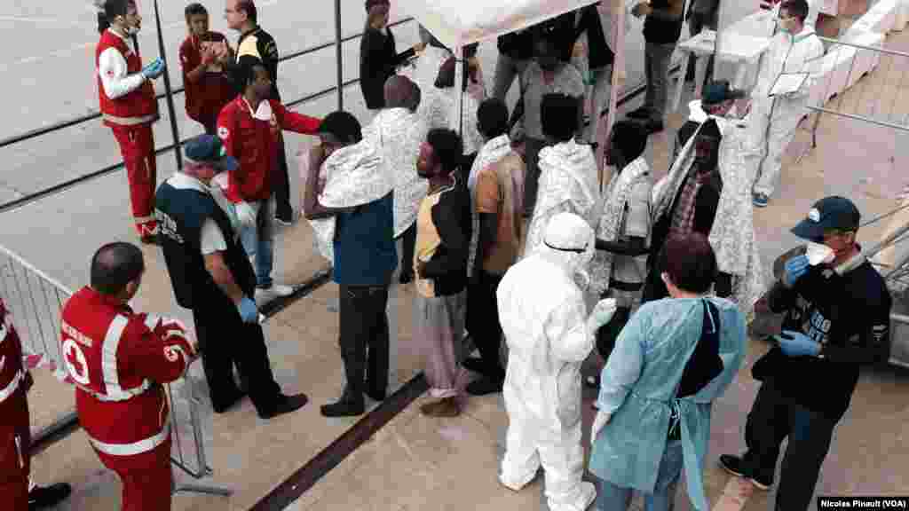 Des volontaires de la Croix rouge et des personnels de santé examinent les migrants à la descente du bateau, Messine, Sicile, 6 octobre 2015 (Nicolas Pinault/VOA).