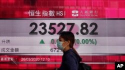 A woman wearing face mask walks past a bank electronic board showing the Hong Kong share index at Hong Kong Stock Exchange Thursday, March 26, 2020.