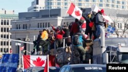 Protesters stand on a trailer carrying logs as truckers and supporters take part in a convoy to protest COVID-19 vaccine mandates for cross-border truck drivers in Ottawa, Ontario, Canada, Jan. 29, 2022.