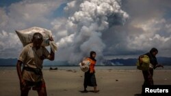 FILE - Smoke is seen on the Myanmar border as Rohingya refugees walk on the shore after crossing the Bangladesh-Myanmar border by boat through the Bay of Bengal, in Shah Porir Dwip, Bangladesh, Sept. 11, 2017. 
