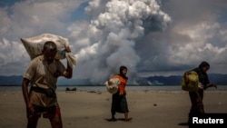 FILE - Smoke is seen on the Myanmar border as Rohingya refugees walk on the shore after crossing the Bangladesh-Myanmar border by boat through the Bay of Bengal, in Shah Porir Dwip, Bangladesh, Sept. 11, 2017. 