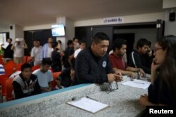 ARCHIVO- Personas deportadas de Estados Unidos esperan para hacer una llamada telefónica a EE.UU. en una instalación de inmigración en San Salvador, El Salvador, el 3 de julio de 2018.