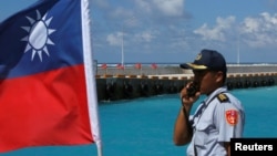 FILE - A member of the Taiwanese Coast Guard stands next to a Taiwanese flag on Itu Aba, which the Taiwanese call Taiping, at the South China Sea, Nov. 29, 2016.