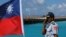 FILE - A member of the Taiwanese Coast Guard stands next to a Taiwanese flag on Itu Aba, which the Taiwanese call Taiping, at the South China Sea, Nov. 29, 2016.