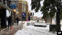 Personas limpian las calles tras una tormenta otoñal de nieve en Helena, Montana, el miércoles 9 de octubre del 2019. (AP Foto/Matt Volz).