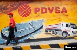 FILE - A worker walks past a mural with a PDVSA logo at its gas station in Caracas, Aug. 29, 2014.